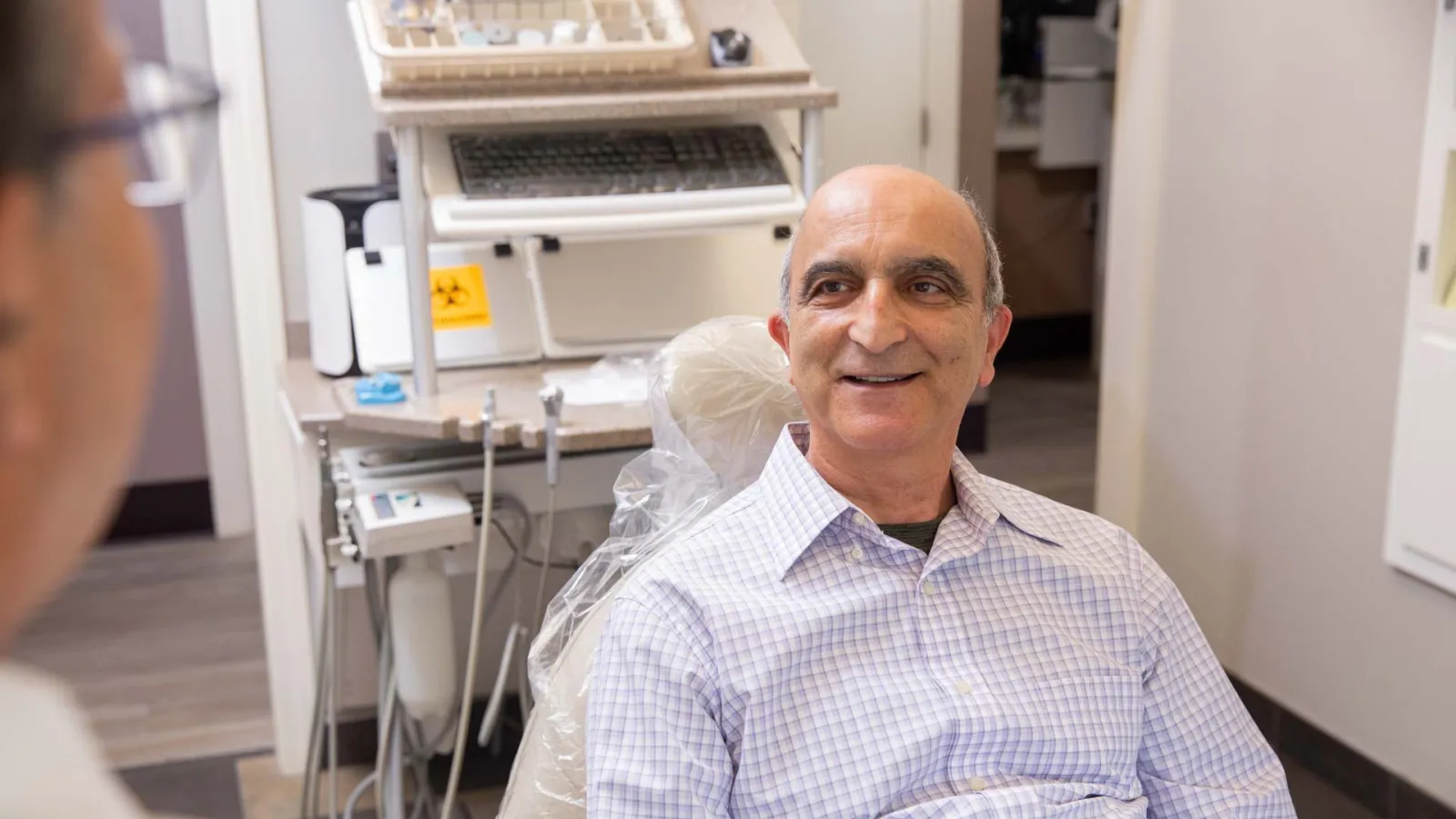 Middle-aged man smiling while sitting in dental chair during consultation with dentist