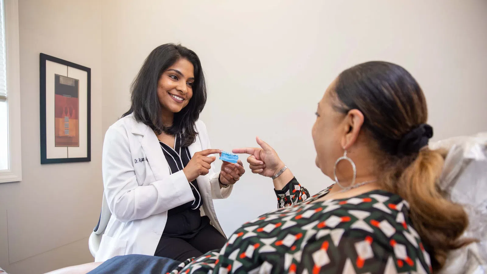 Female doctor explaining dental model to patient in clinic with friendly interaction and consultation.