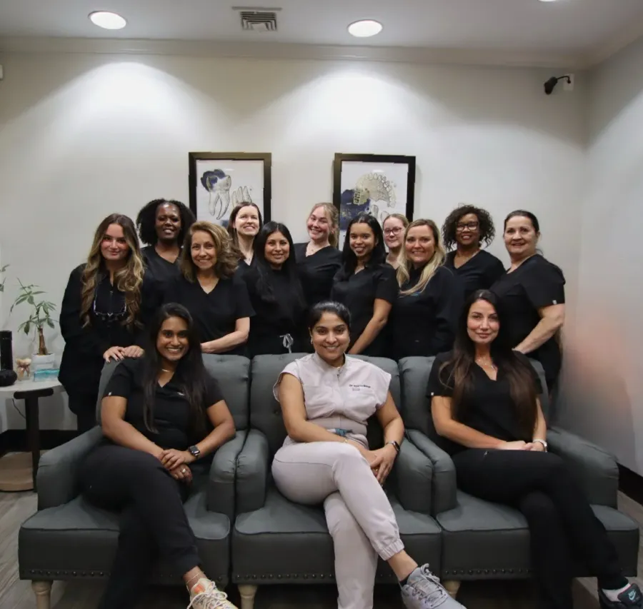 Group of diverse women in black and white uniforms posing together on sofas in a professional setting.